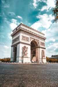 L’Arc de Triomphe se dresse fièrement sous un ciel d’un bleu éclatant, avec ses sculptures finement ciselées et ses rues pavées qui évoquent tout le charme historique de Paris.